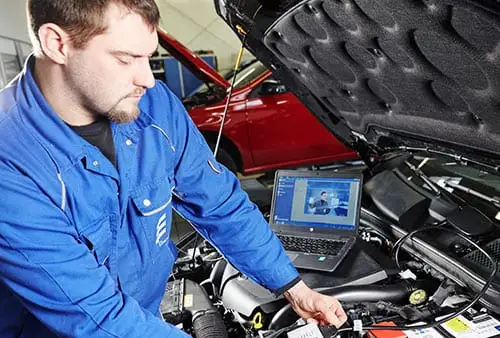 Autolifen asentaja tekee vianmääritystä kannettavalla tietokoneella auton moottoritilassa.